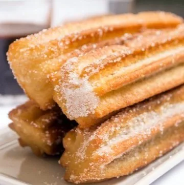 Churros recién fritos y rebozados en azúcar, apilados en un plato
