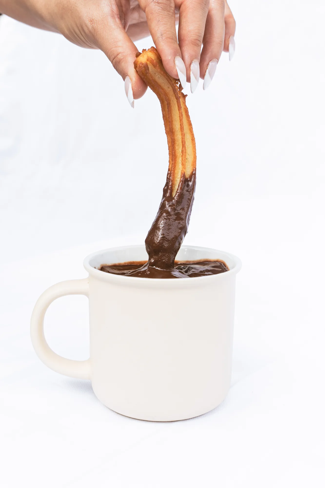 Un churro mojándose en una taza de chocolate artesanal
