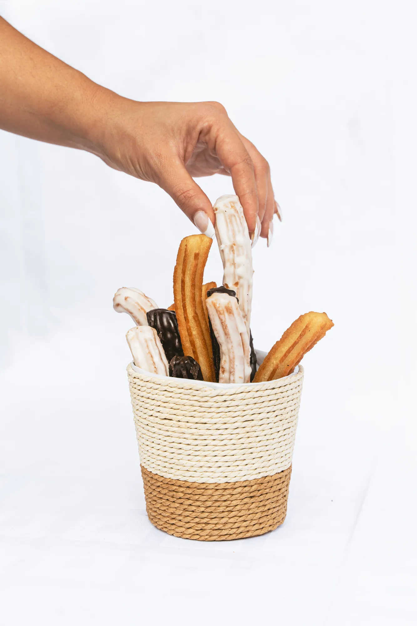 Una mano cogiendo un churro bañado de una cesta de churros artesanos